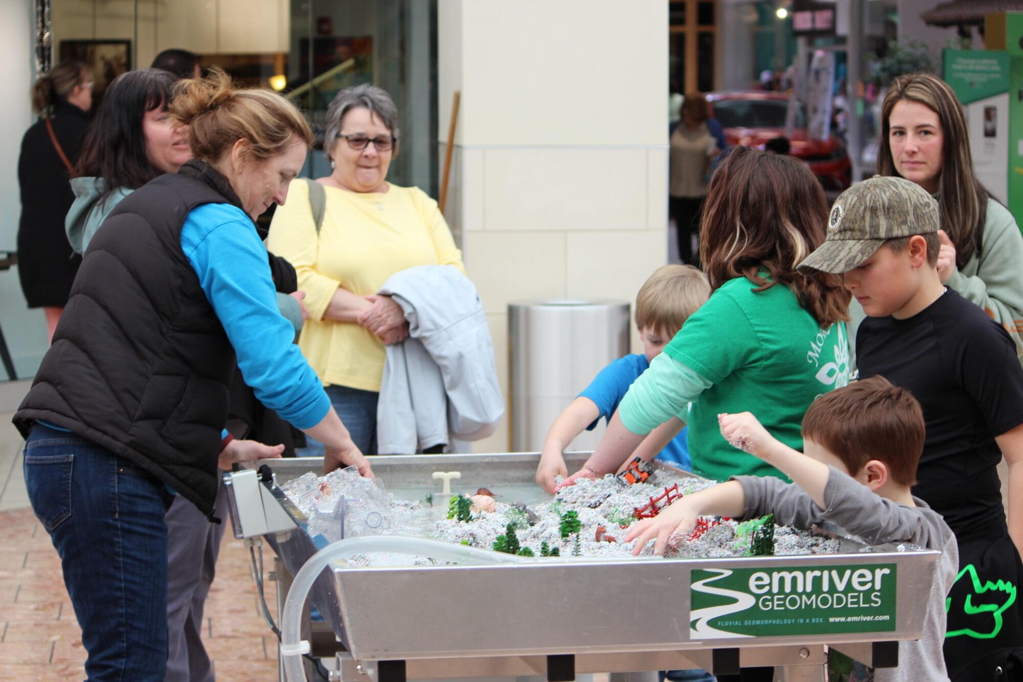 Mall visitors learn about floods and erosion using a hands-on river model.