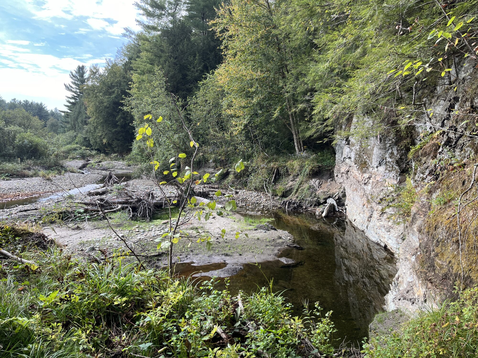 stream with gravel bank on one side and rocky cliff on the other